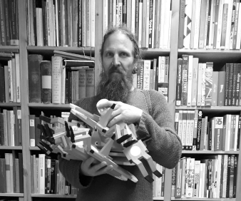 Ein Mann, der viele Fuchsfiguren im Arm hält, steht vor einem Bücheregal